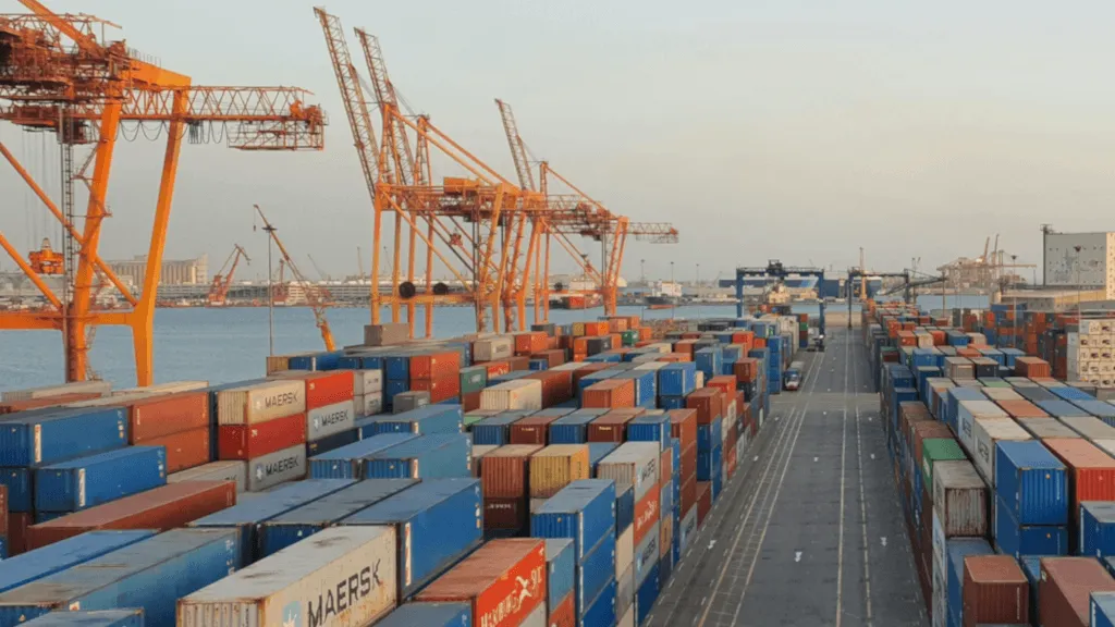 A snowy landscape where colorful shipping containers are standing around, being stacked by big cranes